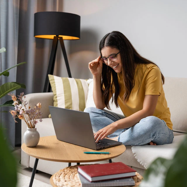 Junge Studentin sitzt gemütlich Zuhause auf Ihrem Sofa und lernt am Laptop