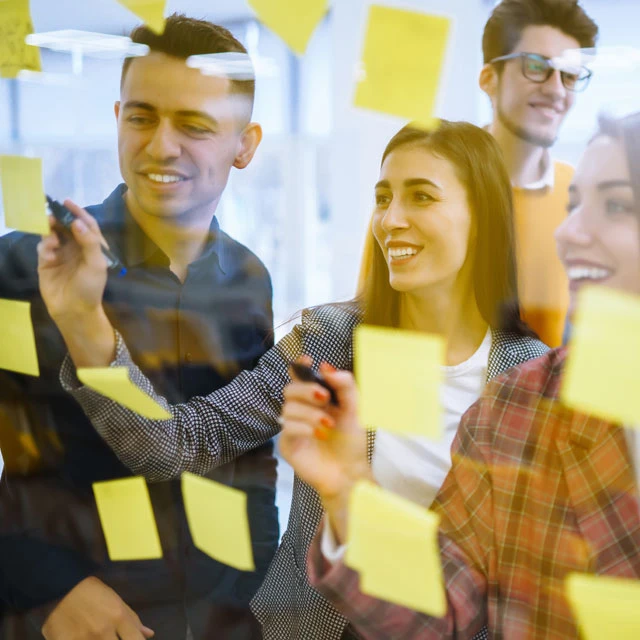 Personengruppe junger Studenten mit Post-Its und Stiften an einer gläsernen Projekttafel