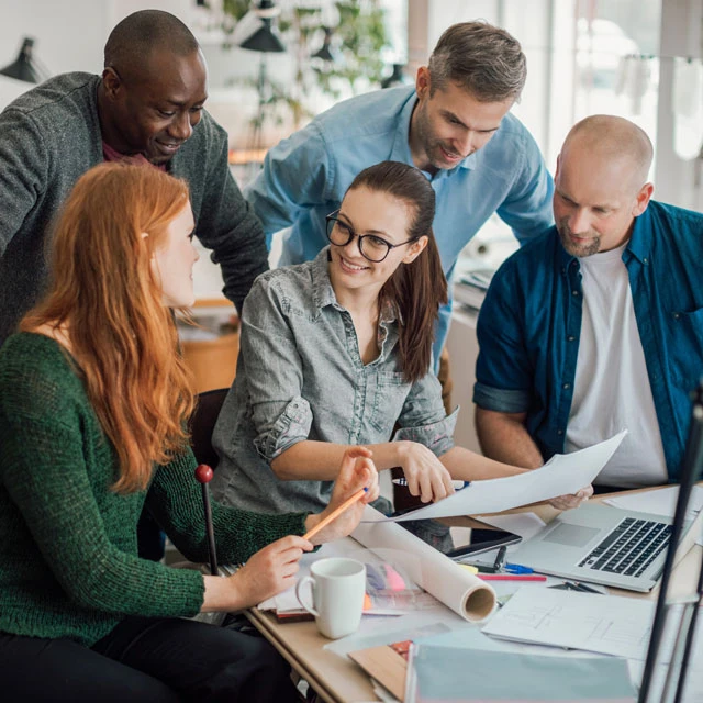 freudig diskutierende Personengruppe versammelt an einem Arbeitsplatz