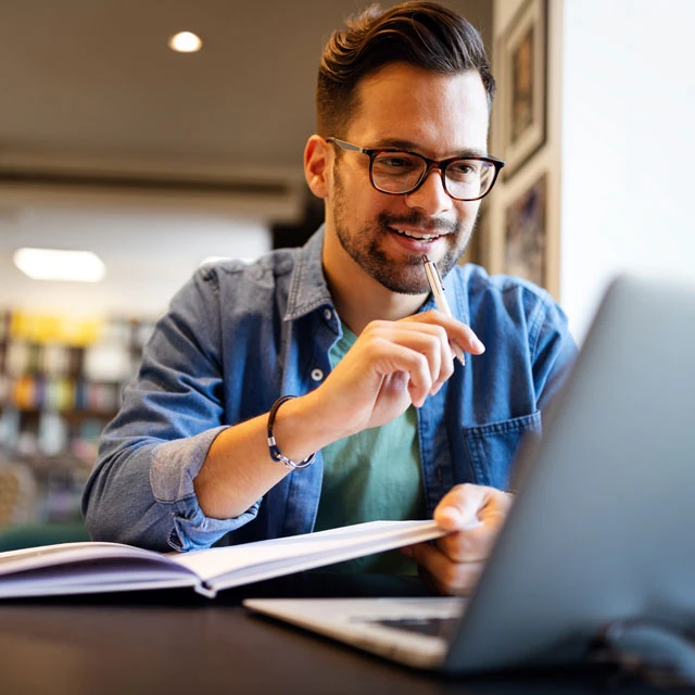 Lächelnder männlicher Student, der in einer Bibliothek arbeitet und studiert